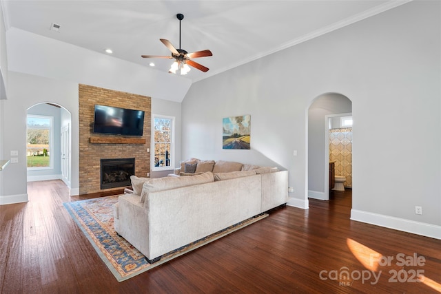 living area featuring arched walkways, lofted ceiling, wood finished floors, baseboards, and a brick fireplace