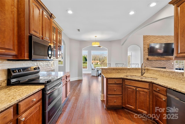 kitchen featuring dark wood-style flooring, decorative backsplash, appliances with stainless steel finishes, a sink, and light stone countertops