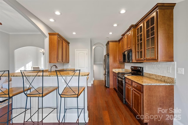 kitchen featuring stainless steel appliances, arched walkways, a kitchen breakfast bar, and light stone counters