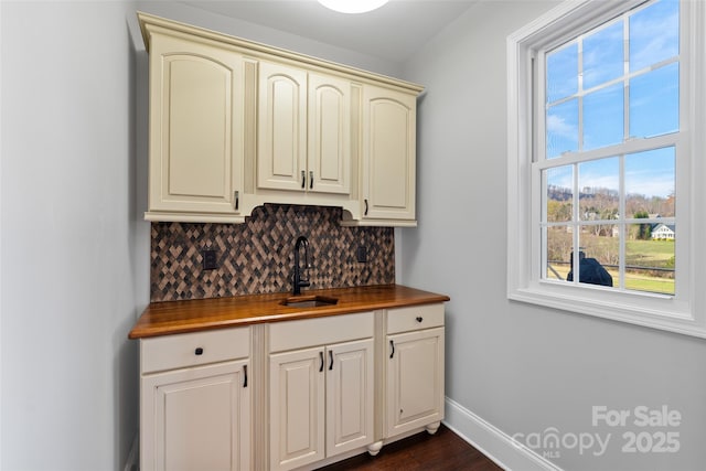 interior space with dark wood-style floors, tasteful backsplash, a sink, and baseboards