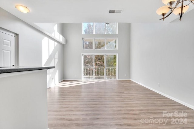 unfurnished living room with a high ceiling, light wood-type flooring, and a notable chandelier