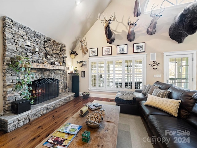 living room featuring a stone fireplace, wood-type flooring, and high vaulted ceiling