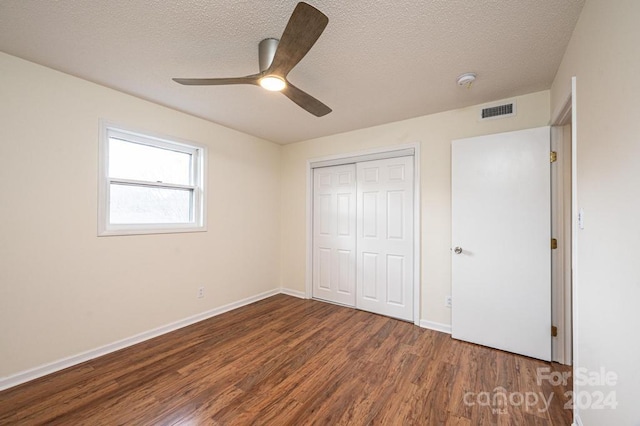 unfurnished bedroom featuring a textured ceiling, a closet, ceiling fan, and dark wood-type flooring