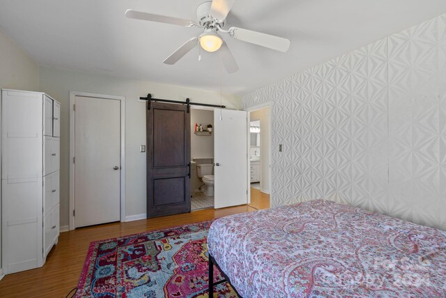 bedroom with ceiling fan, a barn door, light wood-type flooring, and ensuite bathroom