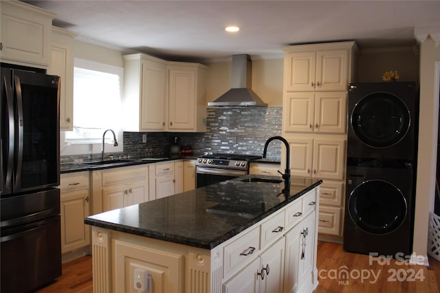 kitchen featuring black fridge, stacked washer / drying machine, wall chimney exhaust hood, and sink