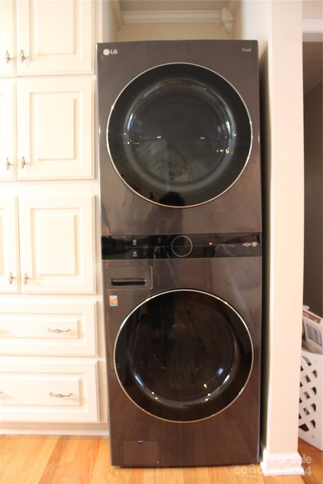 clothes washing area featuring crown molding, light hardwood / wood-style floors, cabinets, and stacked washer / dryer