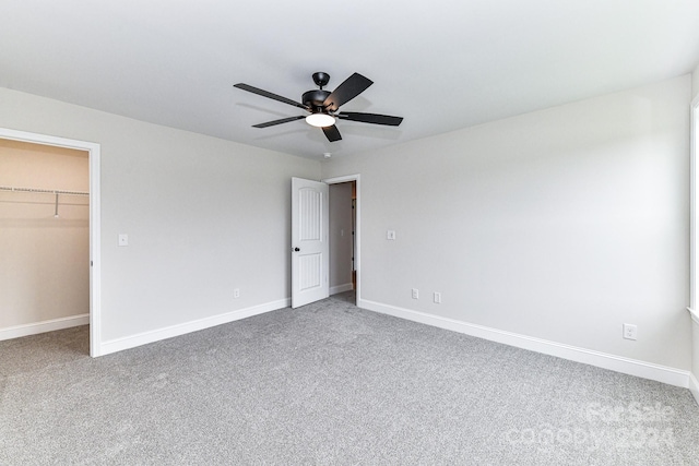 unfurnished bedroom with ceiling fan, a walk in closet, and carpet floors