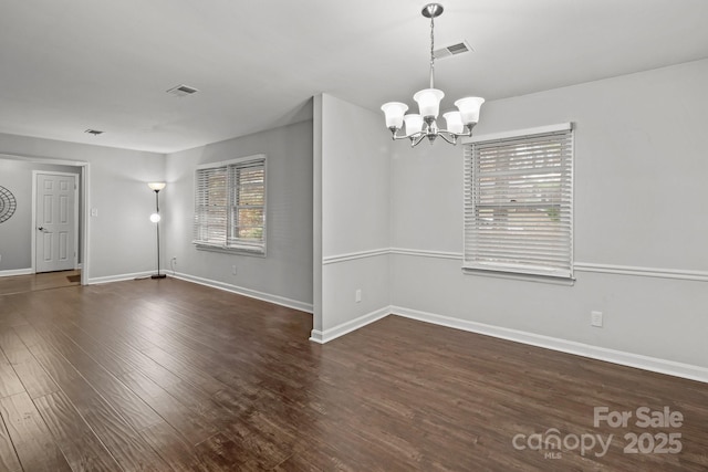 empty room with dark wood-type flooring and a notable chandelier