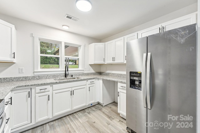 kitchen with light stone countertops, stainless steel fridge, sink, light hardwood / wood-style flooring, and white cabinetry