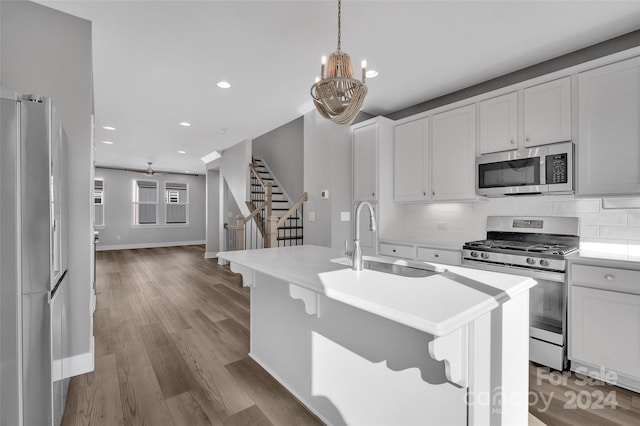 kitchen featuring sink, hanging light fixtures, stainless steel appliances, light hardwood / wood-style flooring, and a center island with sink