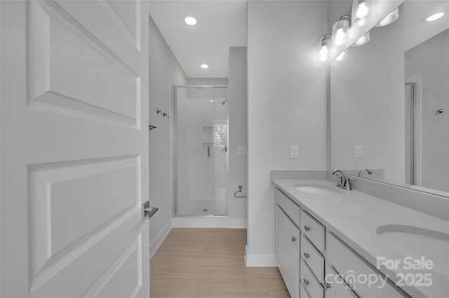 full bath featuring baseboards, double vanity, recessed lighting, a shower stall, and a sink