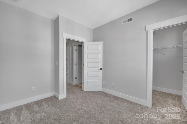 unfurnished bedroom featuring a walk in closet, carpet flooring, baseboards, and visible vents