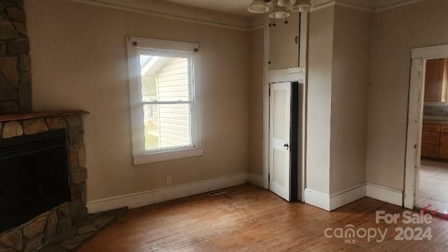 unfurnished living room with ceiling fan, a fireplace, crown molding, and light wood-type flooring