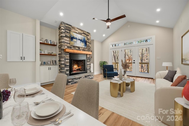 living room featuring a stone fireplace, ceiling fan, light hardwood / wood-style flooring, and high vaulted ceiling