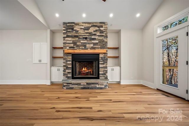 living room featuring light hardwood / wood-style flooring, lofted ceiling, and a stone fireplace