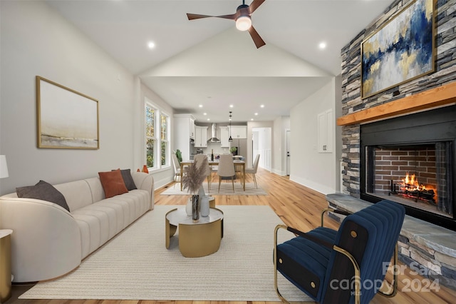 living room with ceiling fan, light hardwood / wood-style floors, a stone fireplace, and high vaulted ceiling