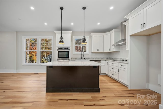 kitchen with a kitchen island, white cabinets, stainless steel appliances, wall chimney exhaust hood, and a sink