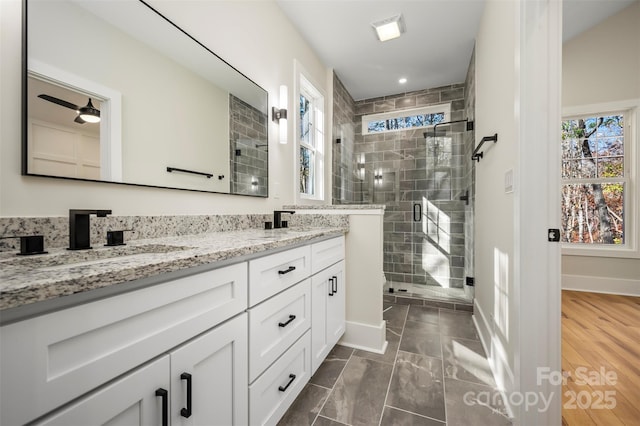 full bathroom with baseboards, double vanity, a stall shower, ceiling fan, and a sink