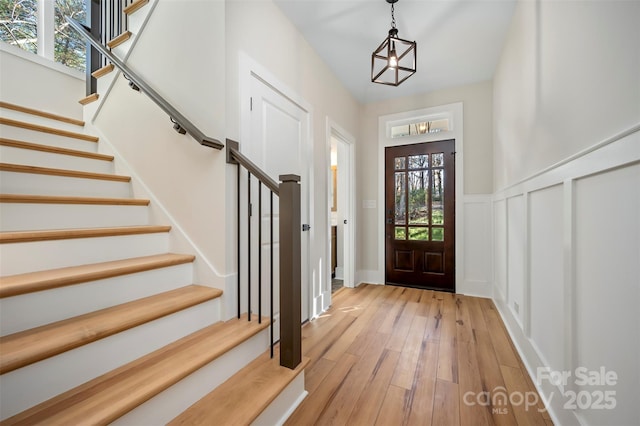 foyer entrance featuring stairs, a decorative wall, light wood-style floors, and wainscoting