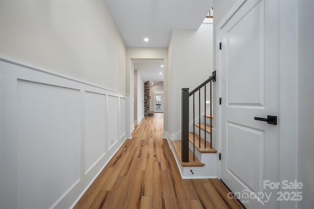 corridor with wood finished floors, recessed lighting, stairway, wainscoting, and a decorative wall