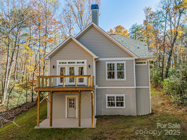 back of property with a patio, a wooden deck, a yard, a chimney, and a shingled roof