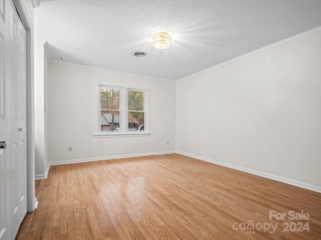 unfurnished room featuring a textured ceiling, light wood-type flooring, and ornamental molding