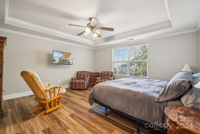 bedroom with hardwood / wood-style floors, ceiling fan, ornamental molding, and a tray ceiling