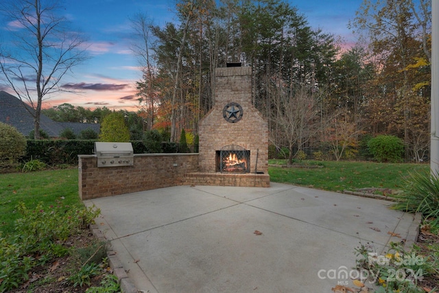 patio terrace at dusk with a lawn, an outdoor brick fireplace, area for grilling, and grilling area