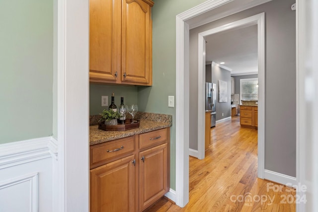 bar featuring stone countertops, stainless steel fridge, ornamental molding, and light hardwood / wood-style flooring