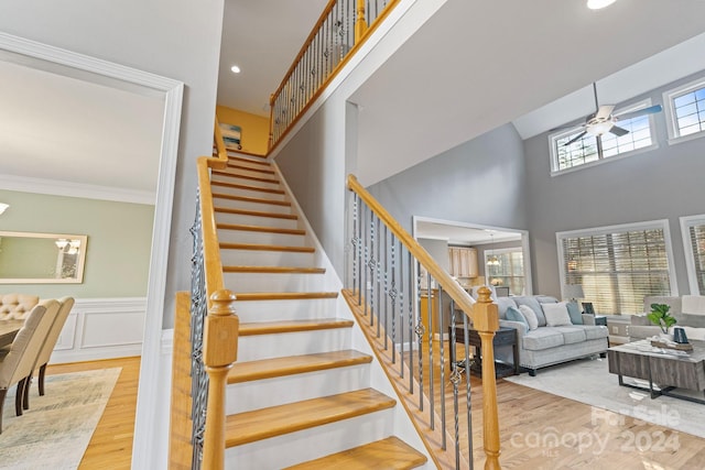 staircase with hardwood / wood-style floors, ceiling fan, ornamental molding, and a high ceiling