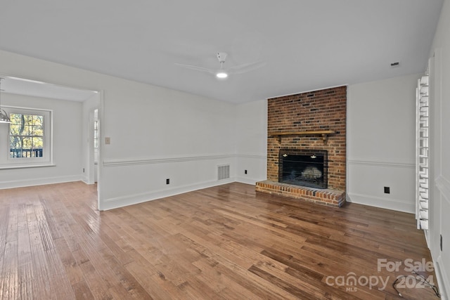 unfurnished living room featuring hardwood / wood-style flooring, a brick fireplace, and ceiling fan