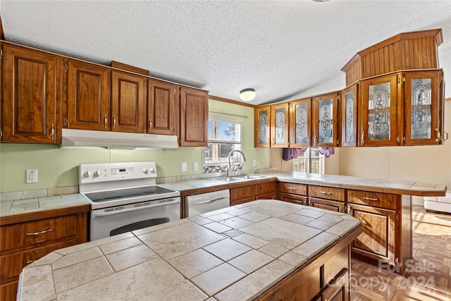 kitchen with a textured ceiling, tile counters, white appliances, and sink