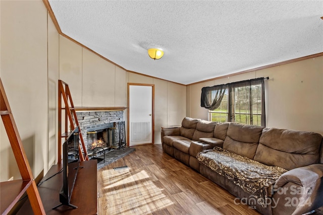 living room featuring lofted ceiling, light hardwood / wood-style flooring, ornamental molding, a fireplace, and a textured ceiling