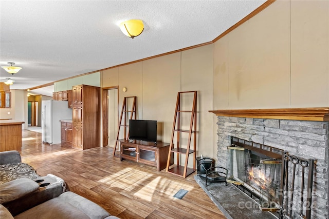 living room featuring a stone fireplace, light hardwood / wood-style floors, a textured ceiling, and ornamental molding