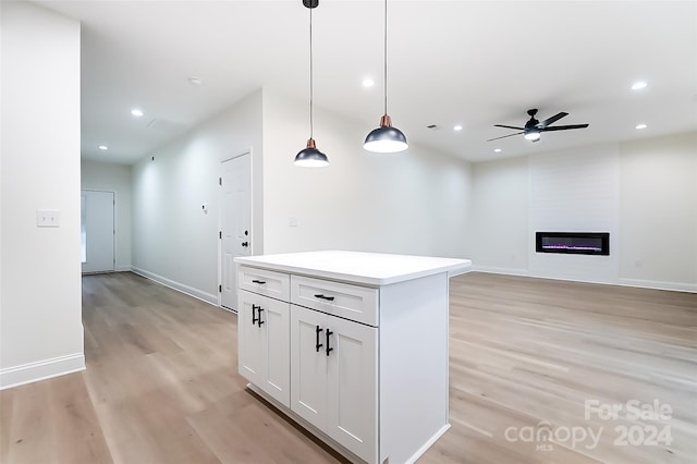 kitchen featuring light wood-type flooring, a large fireplace, ceiling fan, decorative light fixtures, and white cabinets