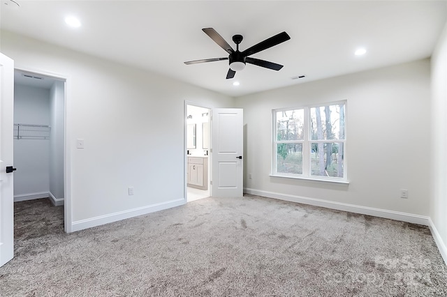 unfurnished bedroom featuring carpet flooring, ensuite bathroom, ceiling fan, a spacious closet, and a closet