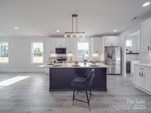 kitchen featuring appliances with stainless steel finishes, pendant lighting, wine cooler, white cabinets, and a center island