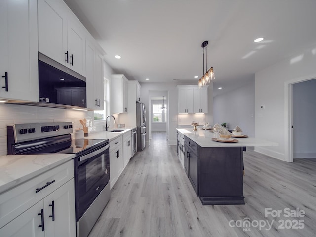 kitchen with sink, appliances with stainless steel finishes, white cabinetry, hanging light fixtures, and light stone countertops