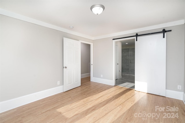 unfurnished bedroom featuring a barn door, ensuite bath, and light hardwood / wood-style floors