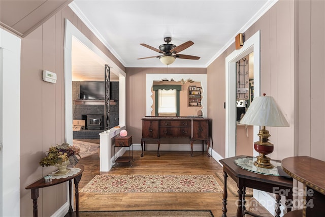 interior space featuring a wood stove, ceiling fan, wood-type flooring, and ornamental molding