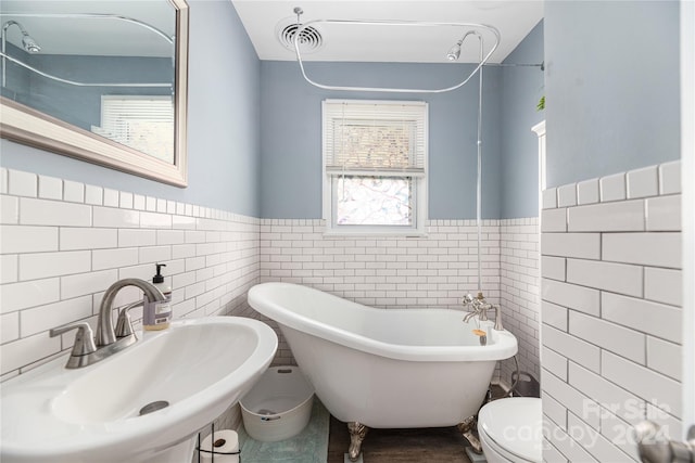 bathroom with toilet, tile walls, a bathing tub, and sink