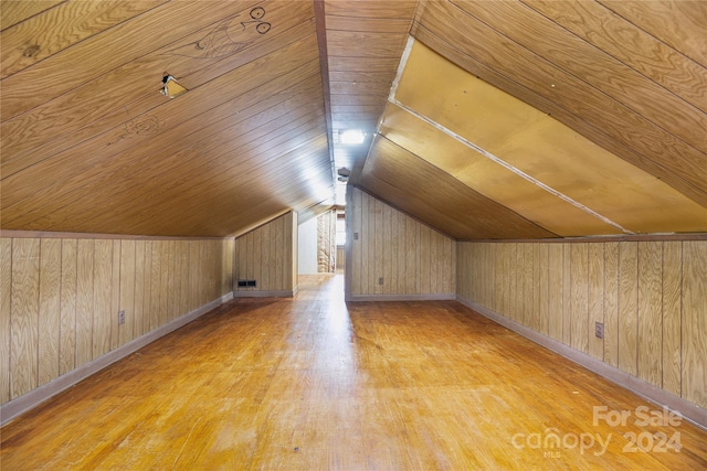 additional living space featuring lofted ceiling, light wood-type flooring, and wooden walls