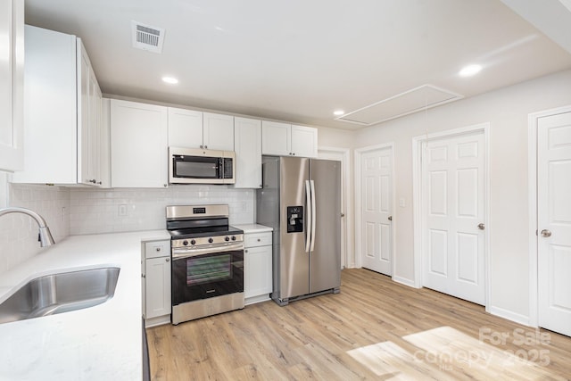 kitchen featuring white cabinets, sink, light hardwood / wood-style flooring, appliances with stainless steel finishes, and tasteful backsplash