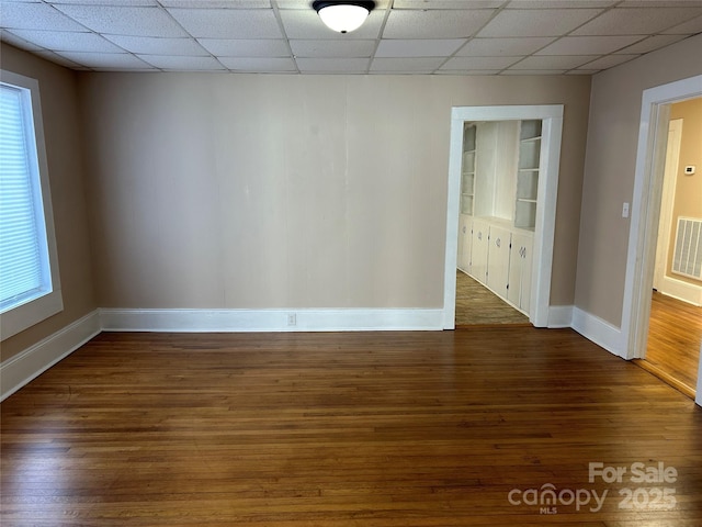 unfurnished room with dark wood-type flooring, built in features, and a drop ceiling