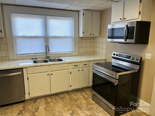 kitchen with sink, a paneled ceiling, appliances with stainless steel finishes, backsplash, and white cabinets