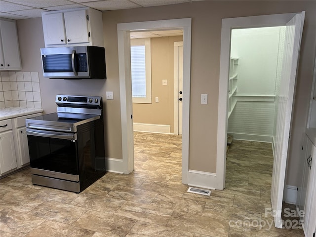 kitchen with stainless steel appliances, tasteful backsplash, a drop ceiling, and white cabinets