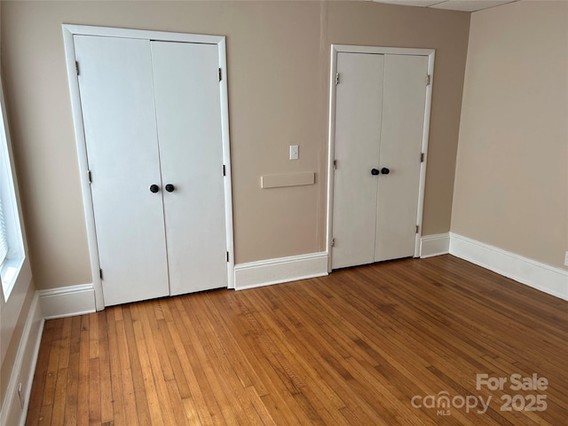 unfurnished bedroom with hardwood / wood-style flooring and multiple closets