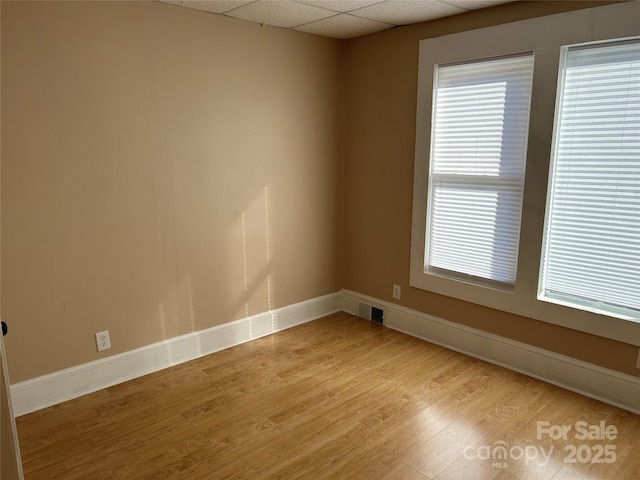 empty room with a drop ceiling and light hardwood / wood-style floors