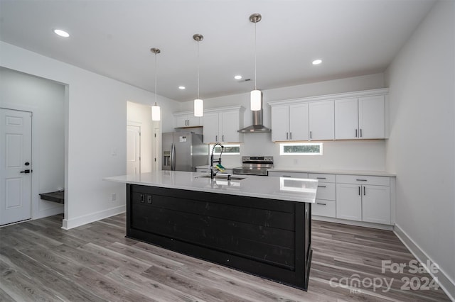 kitchen featuring stainless steel appliances, a kitchen island with sink, wall chimney range hood, sink, and white cabinetry