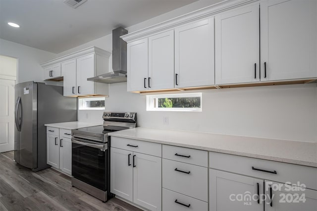 kitchen with white cabinets, appliances with stainless steel finishes, light hardwood / wood-style flooring, and wall chimney range hood